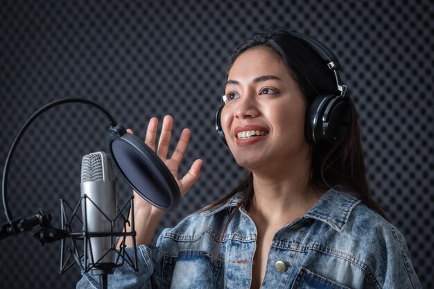 Felice allegro piuttosto sorridente del ritratto di una giovane cantante asiatica che indossa le cuffie che registra una canzone davanti al microfono in uno studio professionale