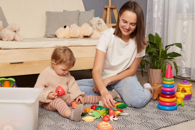 Felice amorevole giovane madre caucasica gioca con i giocattoli frutta di plastica con la piccola figlia Felice mamma sorridente si diverte a sentirsi giocosa con il piccolo bambino bambino Parenthood