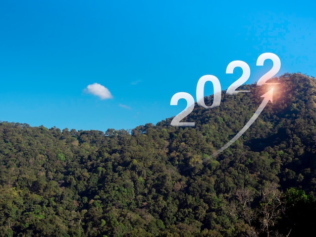 Felice anno nuovo 2022 con grandi lettere sulle lussureggianti montagne verdi e freccia in aumento con brillante, concetto di obiettivo aziendale. Benvenuto, Buon Natale e Felice Anno Nuovo nel 2022.