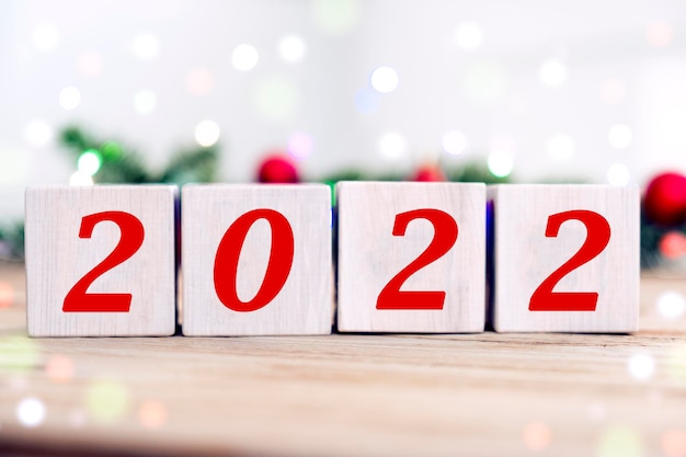 Felice Anno Nuovo 2022 su blocchi di cubo di legno con rami di abete e luci bokeh sfocate sullo sfondo. Biglietto di auguri per le vacanze invernali e buon Natale.