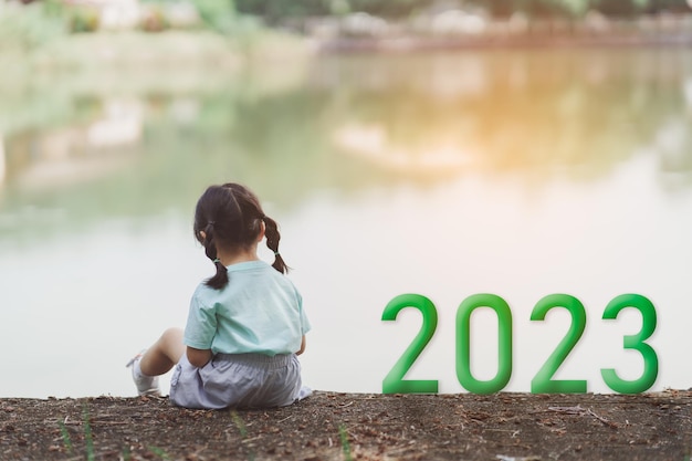 Felice anno nuovo 20232023 simboleggia l'inizio del nuovo anno La lettera inizia il nuovo anno 2023 sul bambino seduto sul pavimento vicino al fiume nel parco naturale Obiettivo del successo Numero 2023 carta da parati