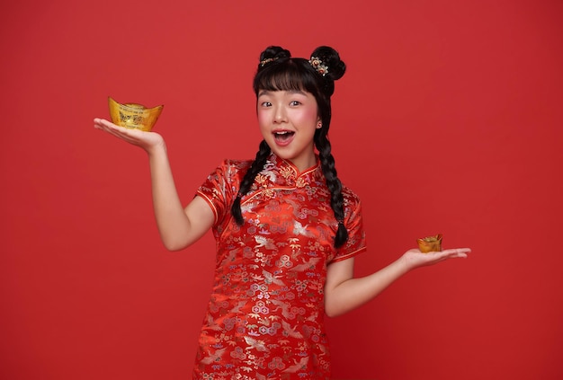 Felice anno nuovo cinese bambini ragazza asiatica che indossa il tradizionale abito qipao tenendo in mano lingotto d'oro