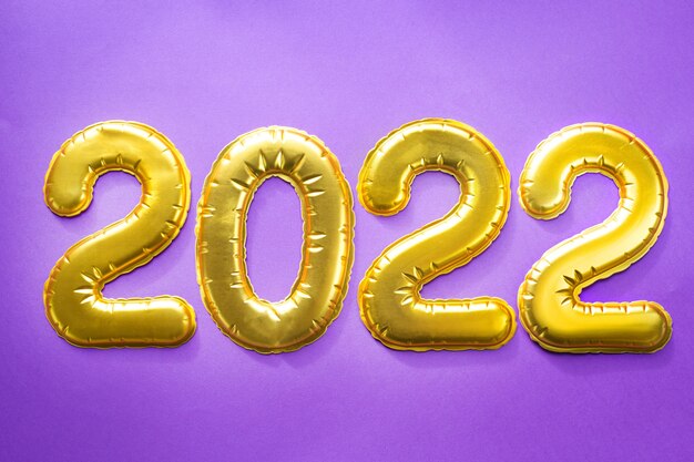 Felice Anno Nuovo - numeri dorati 2022 su sfondo viola con paillettes, stelle, glitter, luci di ghirlande. Saluti, cartolina. Calendario, copertina.
