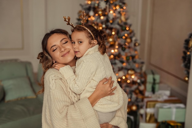 Felice anno nuovo tradizioni familiari la giovane madre e sua figlia si divertono a casa vicino all'albero di Natale e al camino