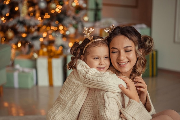 Felice anno nuovo tradizioni familiari la giovane madre e sua figlia si divertono a casa vicino all'albero di Natale e al camino