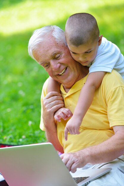 felice anziano senior nonno e bambino nel parco utilizzando il computer portatile