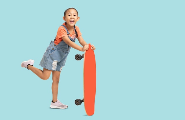 Felice asiatica sorridente bambina che tiene lo skateboard Ritratto completo del corpo isolato su sfondo azzurro chiaro pastello