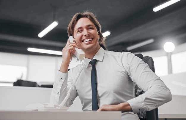 Felice assistente maschio che parla al telefono in ufficio