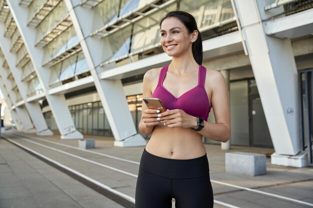 Felice attraente sportiva in posa con lo smartphone all'aperto