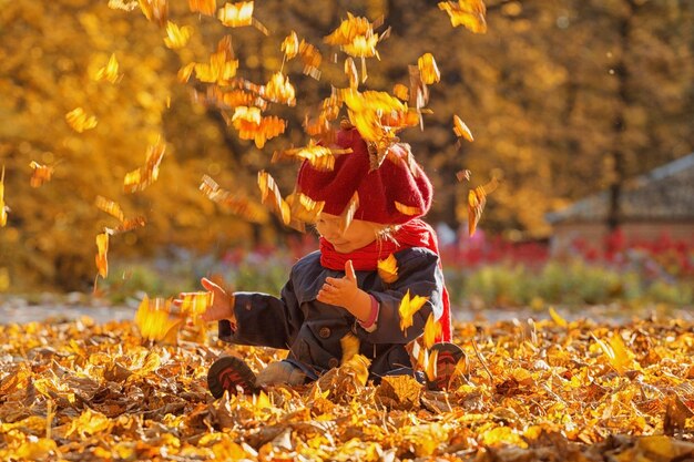 Felice autunno Una bambina con un berretto rosso sta giocando con le foglie che cadono e ridendo