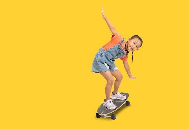 Felice bambina asiatica che gioca a skateboard Ritratto di tutto il corpo isolato su sfondo giallo con percorso di ritaglio per il lavoro di progettazione