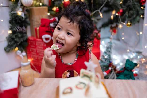 Felice bambina asiatica con torta di Natale a casa in vacanza invernale con la famiglia.