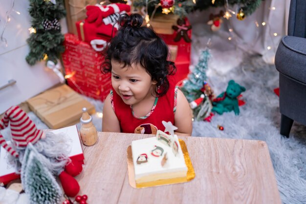 Felice bambina asiatica con torta di Natale a casa in vacanza invernale con la famiglia.