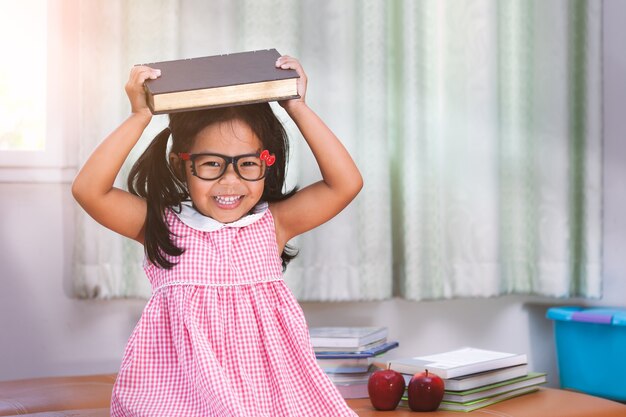 Felice bambina asiatica mettendo il libro sulla sua testa