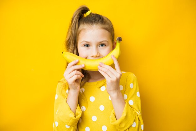 Felice bambina bambino con banana gialla come sorriso su sfondo giallo