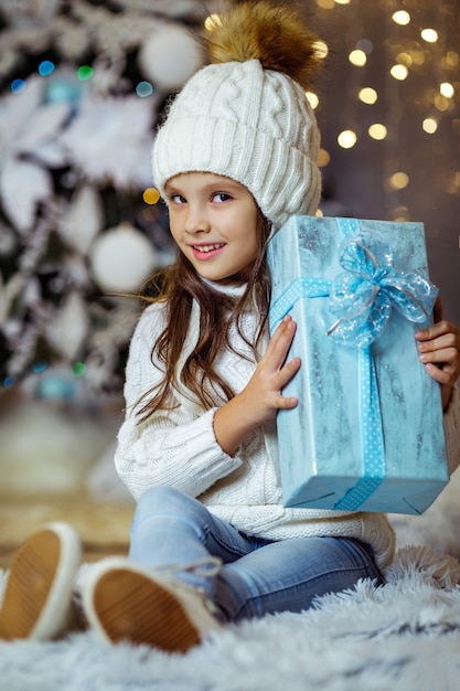 Felice bambina bambino con confezione regalo blu seduto vicino all'albero di Natale decorato con luce