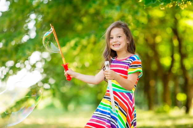 Felice bambina bruna che gioca con le bolle di sapone nel parco