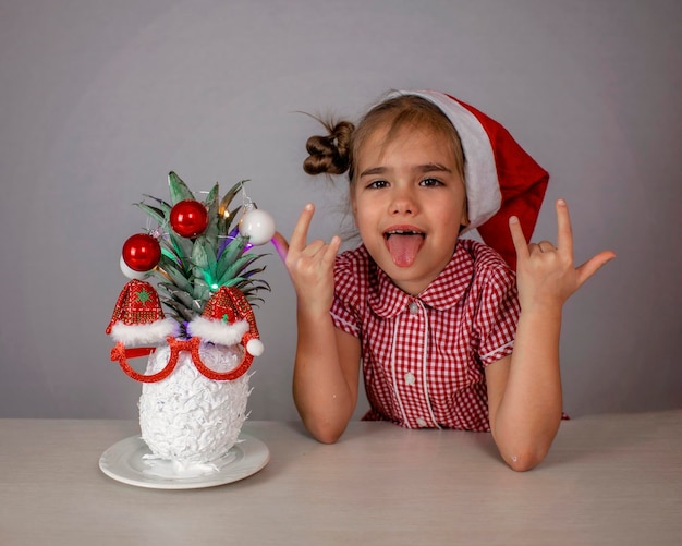 Felice bambina carina vicino al volto di babbo natale fatto con ananas