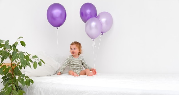 Felice bambina caucasica bambino di 12 anni seduto sul letto con palloncini di colore molto alla moda peri su sfondo bianco in interni moderni scandinavi a casaBambino che si diverteCopia spazio