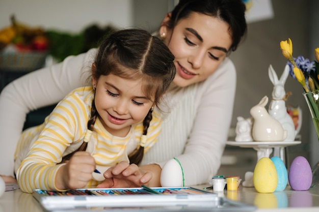 Felice bambina che ride foto di pittura con la mamma al tavolo in cucina Vacanze di Pasqua Tempo di primavera