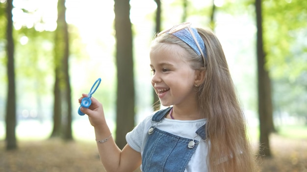 Felice bambina che soffia bolle di sapone fuori nel parco verde. Attività estive all'aperto per il concetto di bambini.