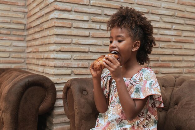 Felice bambina nera che mangia un delizioso croissant