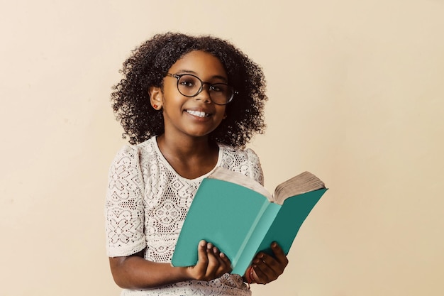 Felice bambina nera con gli occhiali in possesso di un libro