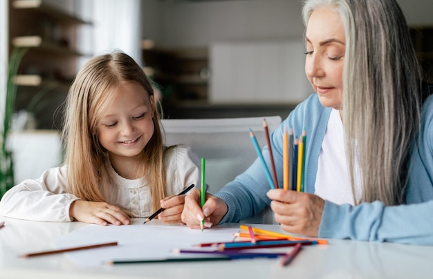 Felice bambino in età prescolare caucasico con nonna in pensione con matite colorate disegnare un'immagine sul tavolo godersi il tempo libero