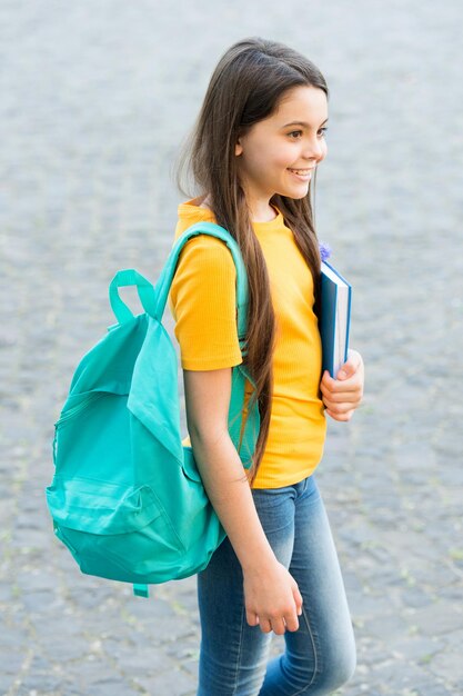 Felice bambino torna a scuola portando zaino e libro in stile casual all'aperto, conoscenza.