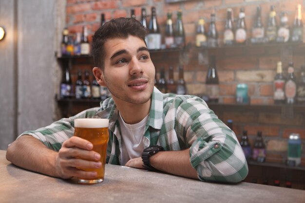 Felice bel giovane godendo di birra al pub, copia dello spazio