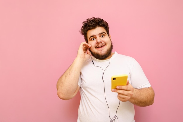 Felice bell'uomo grasso in cuffia e con lo smartphone in mano isolato su sfondo rosa