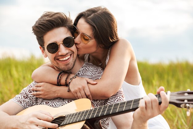 Felice bella coppia seduta al parco insieme, suonando la chitarra, rilassante