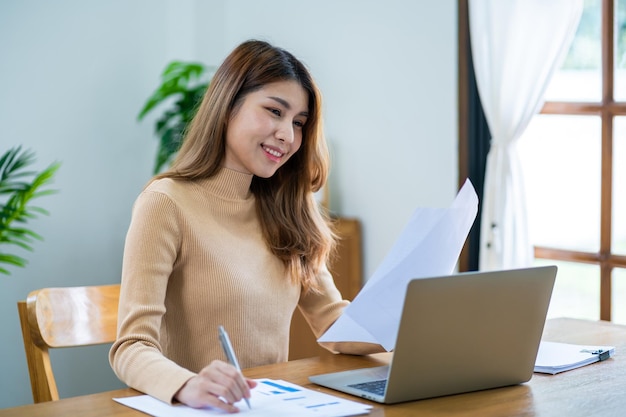 Felice bella donna asiatica donna d'affari che lavora da casa con il portatile finanziario concetto di spazio di lavoro a casa