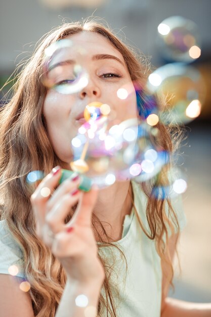 Felice bella donna che soffia bolle di sapone all'aperto