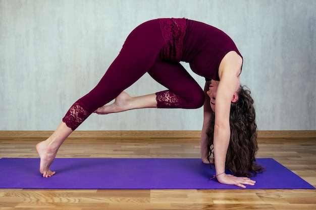 Felice bella donna con capelli ricci che pratica yoga su una stuoia di yoga su un muro grigio sfondo concetto di salute pratica yoga e stretching