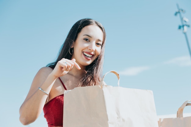 Felice bella donna moderna africana che guarda dentro la borsa della spesa curiosa di sapere cosa c'è dentro. Sul centro commerciale della città. Copia spazio, shopping natalizio per il nuovo anno presenta il concetto, nuova giornata per lo shopping di vestiti.