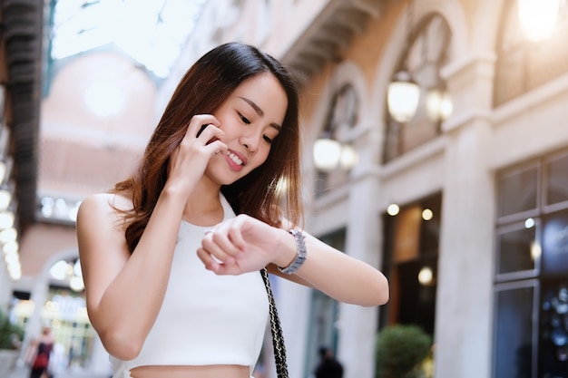 Felice bella donna parlando con qualcuno sul suo telefono cellulare e controllando il tempo