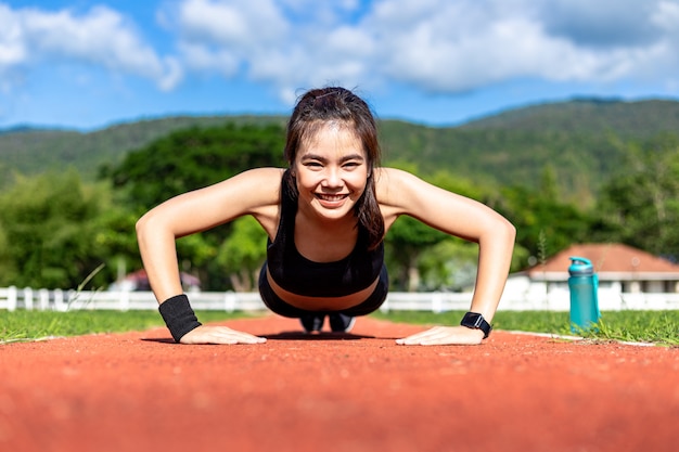 Felice bella giovane donna asiatica facendo push up esercizio al mattino su una pista da corsa in una luminosa giornata di sole