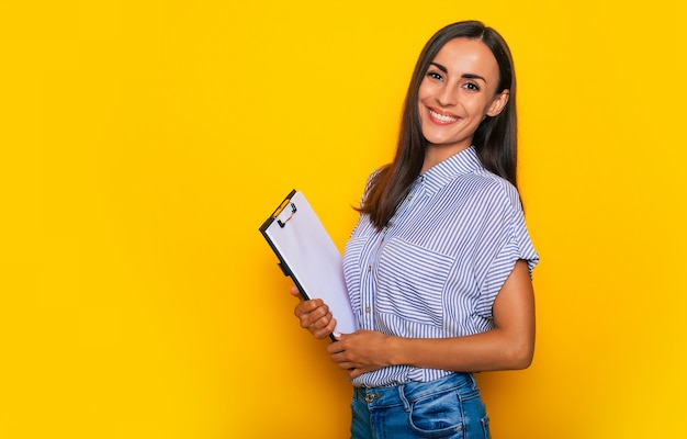 Felice bella giovane donna bruna sicura di sé in elegante abbigliamento casual elegante è in posa su sfondo giallo