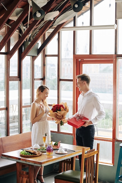 Felice bella giovane donna che accetta bouquet di fiori e presente dal fidanzato