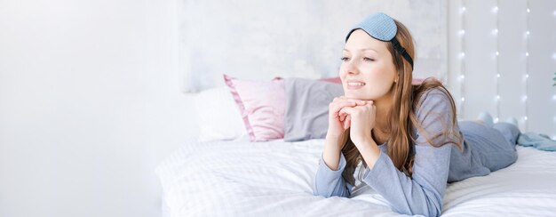 Felice bella giovane donna in buona salute che indossa la maschera del sonno e il pigiama blu sveglio