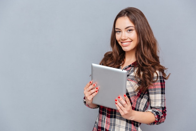 Felice bella giovane donna in camicia a quadri che tiene tablet