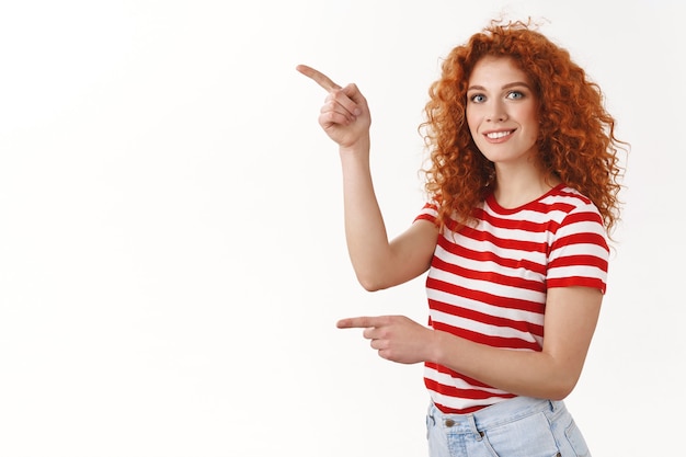 Felice bella rossa riccia donna femminile t-shirt a righe che punta l'indice sinistro guarda la telecamera divertita sorride chiedendo consiglio facendo scelta, raccogliendo prodotti negozio