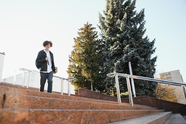 Felice bello studente di college universitario o giovane allievo di scuola ragazzo intelligente di successo con libri libri di testo sorridente all'aperto al tramonto Copia spazio