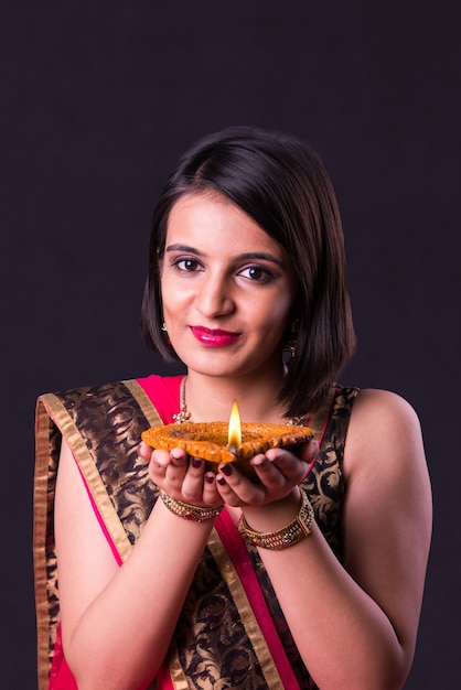 Felice biglietto di auguri diwali che mostra una bella ragazza indiana con in mano una lampada a olio diya o terracotta su sfondo nero