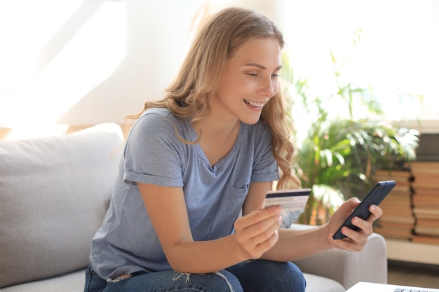 Felice bionda naturale con carta di credito e telefono cellulare in soggiorno.