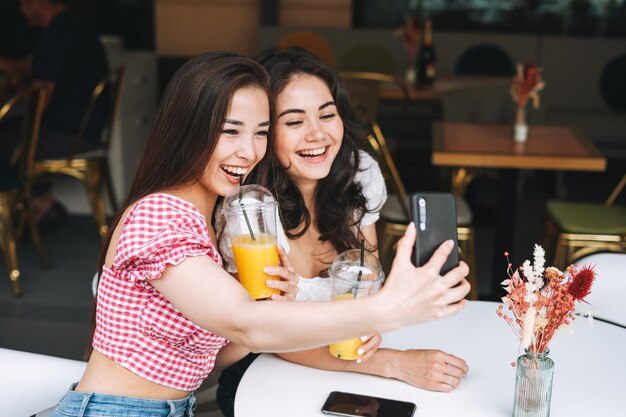 Felice bruna giovani ragazze amici in abiti estivi con succo d'arancia prendere selfie sul telefono cellulare