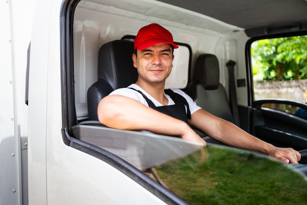 Felice camionista professionista con il suo assistente che indossa un berretto rosso che sorride guardando la telecamera dal finestrino di un camion prima di consegnare il pacco Un camionista e un concetto di servizio di consegna