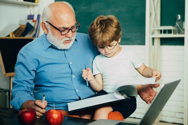 Felice carino ragazzo intelligente e vecchio tutor con libro Divertente bambino divertirsi su sfondo lavagna Un nonno e un bambino stanno imparando in classe