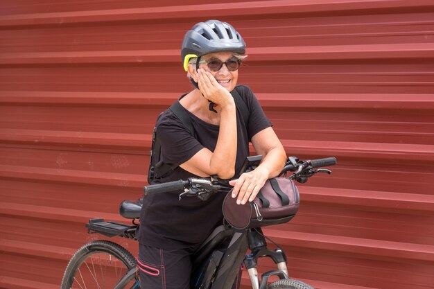 Felice ciclista donna anziana in escursione all'aperto vicino a un pannello di metallo rossostile di vita sano